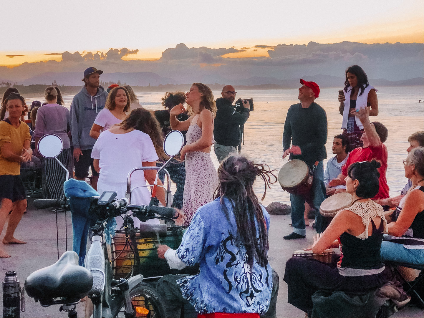 People enjoying and dancing at a drum circle at sunset at main beach in Byron Bay