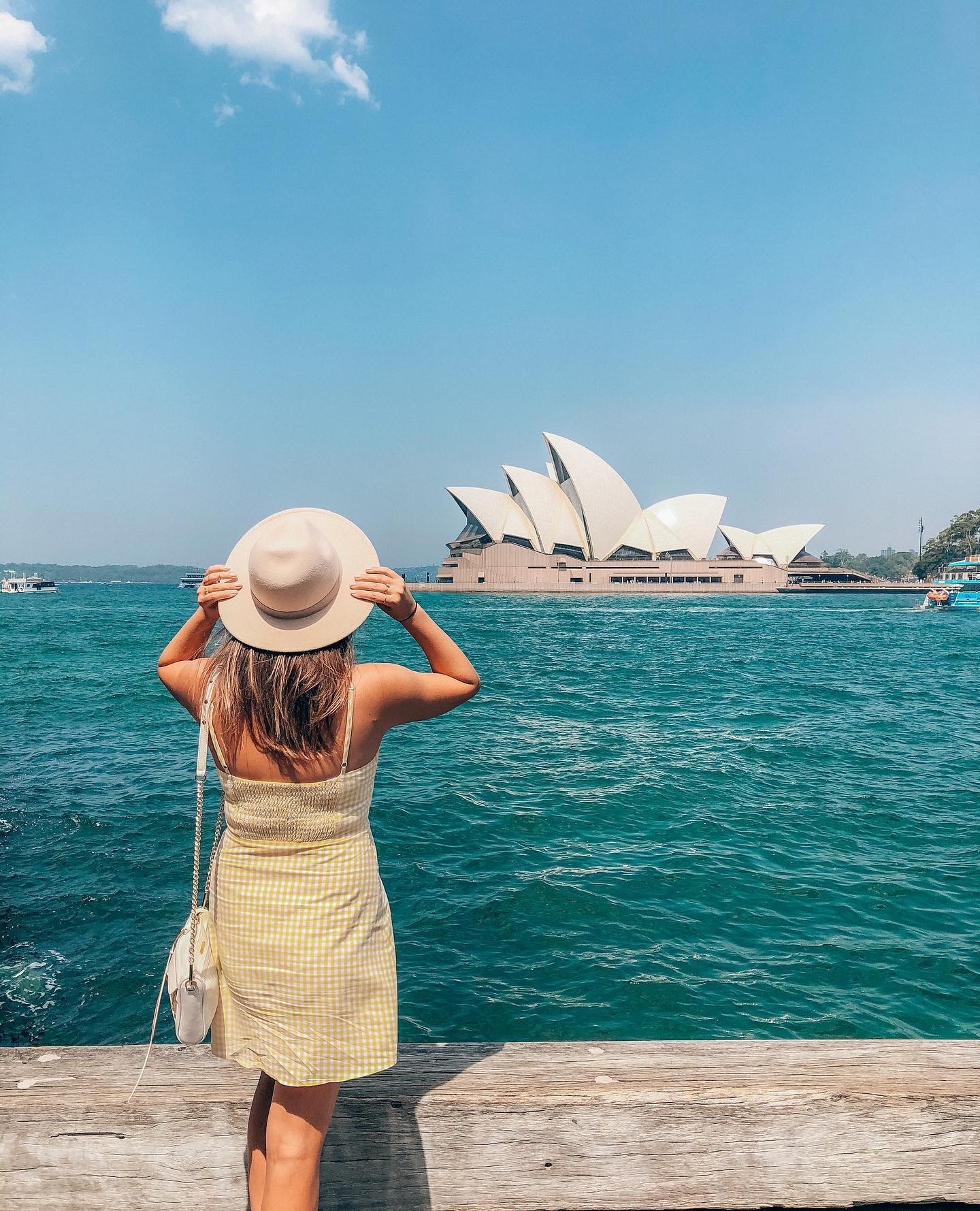 A girl wearing a hat and dress looks at the iconic Sydney Opera House from across the water. A must see during your 24 hours in Sydney, Australia