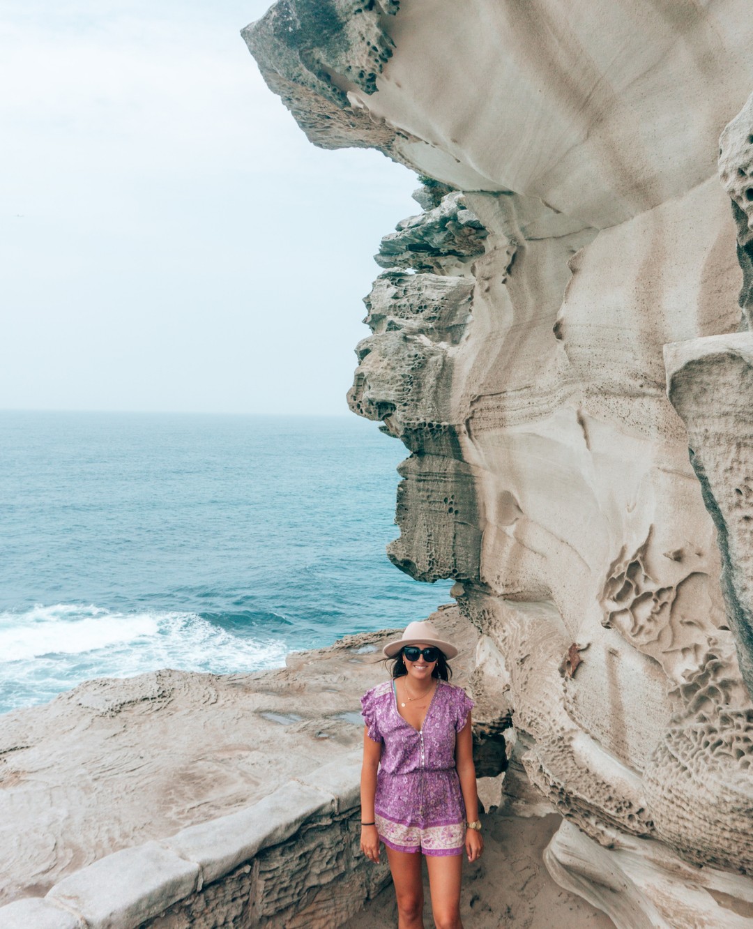 A girl in  a purple romper stands beside an interesting rock formation along the Bondi to Coogee Coastal Trail