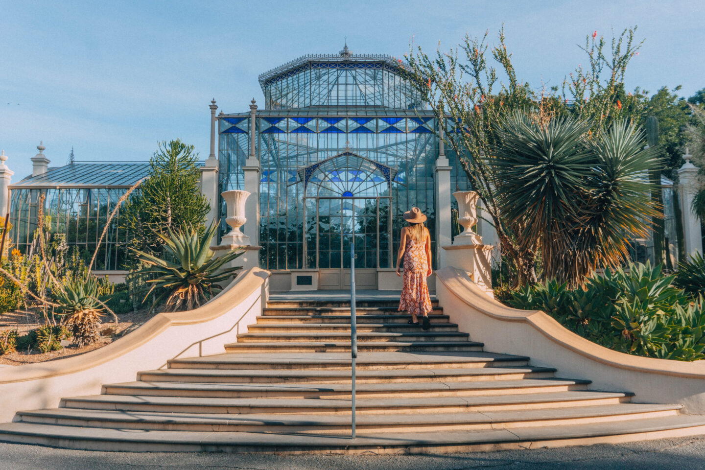 A girl in a dress walks up to the Palm house in Adelaide Botanic Garden with lush greenery surrounding it – best free things to do in Adelaide