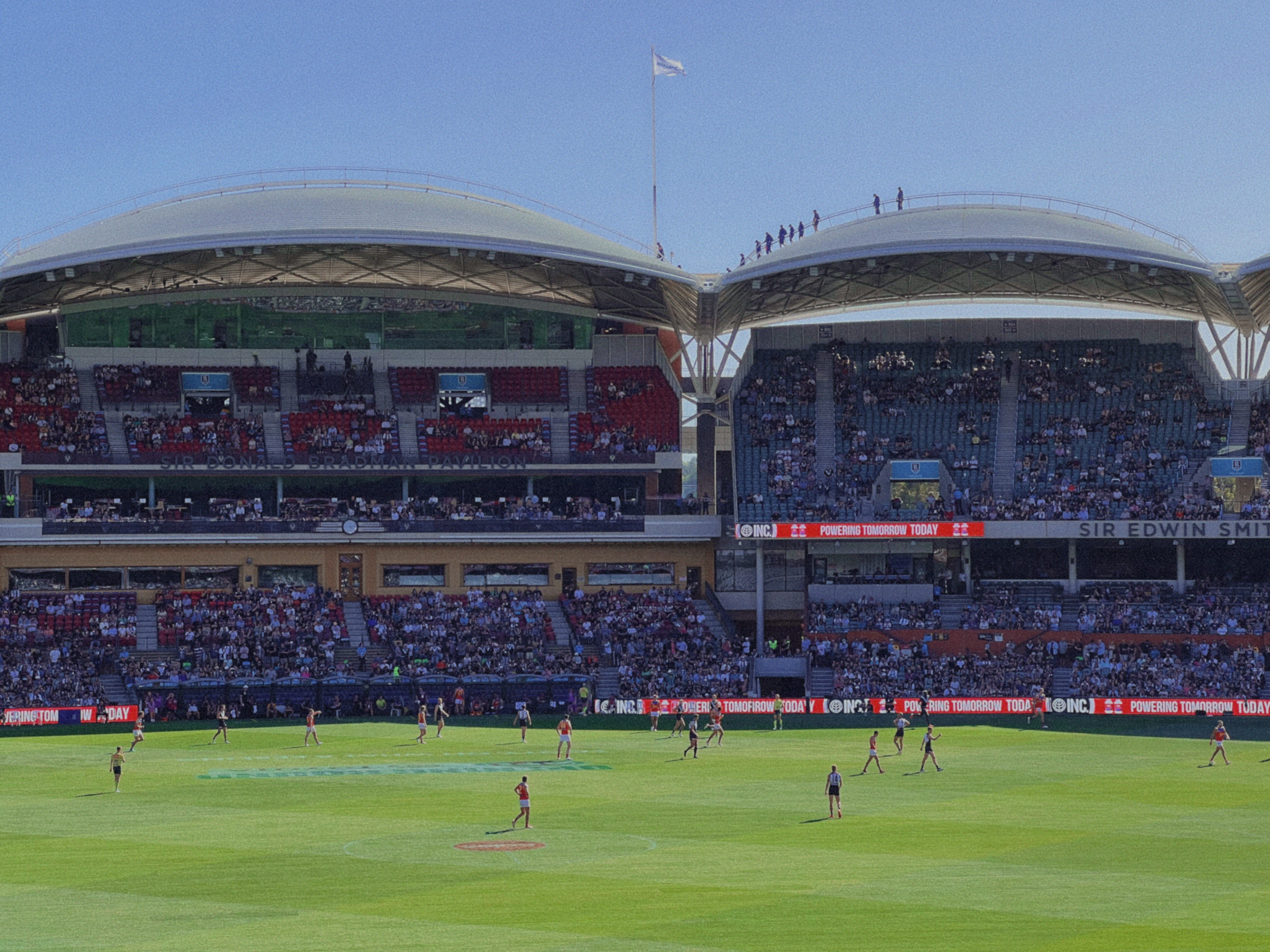 Crowd cheering at Adelaide Oval during an Aussie Rules footy game, while people climb on the roof – fun cultural things to do in Adelaide.