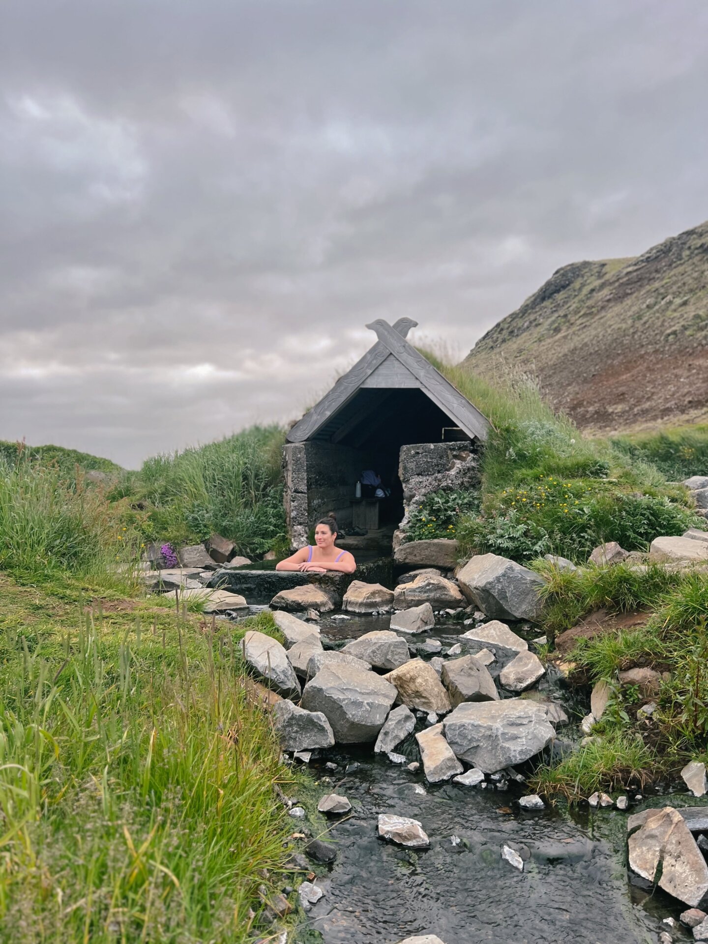 A girl sitting in the Hrunalaug Hot Springs under the authenic hut and taking in the spectacular Icelandic views 